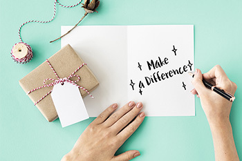 Person writing out "make a difference" on a holiday card