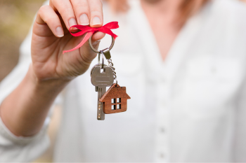 A person holds a house-shaped keychain with a red bow, symbolizing home ownership.