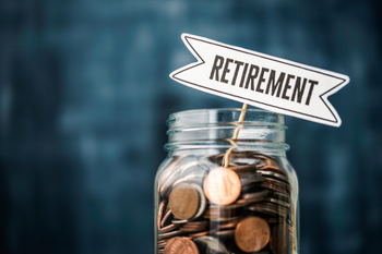 Glass jar filled with coins and topped by a “RETIREMENT” sign, symbolizing savings, financial planning, and hopeful preparation for the future.