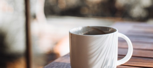Mug of coffee on wooden table overlooking blurred landscape.