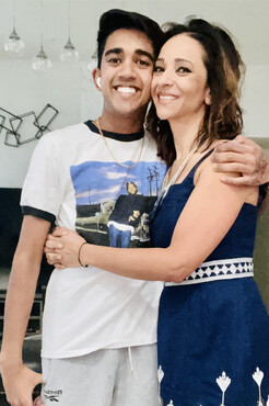 Photo of middle-aged woman with medium length brown hair in a blue and white dress hugging a teenaged male in a t-shirt - Gagan Mausan and her son 
