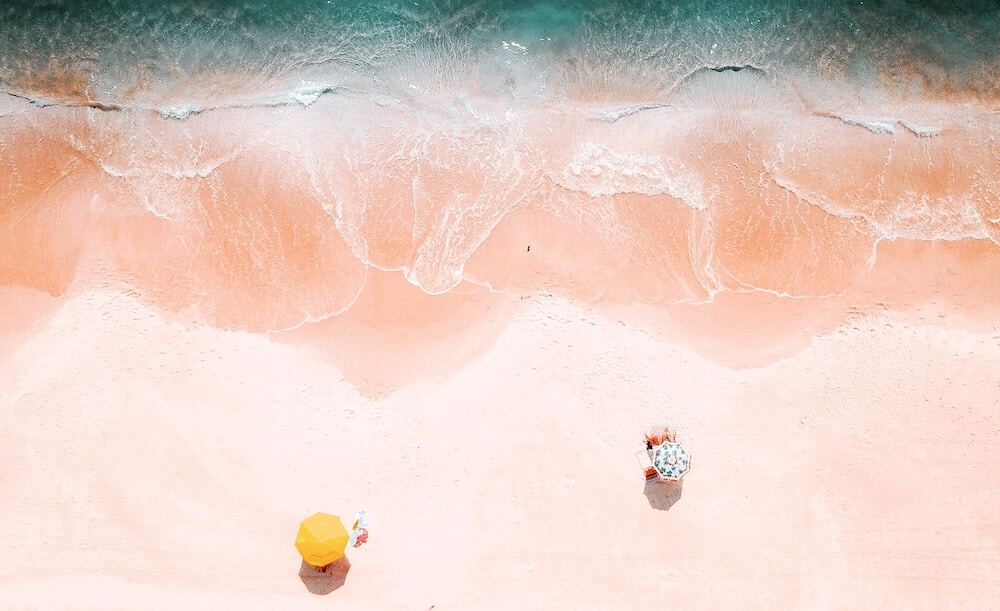 overhead photo of a beach with waves coming in and an umbrella next to a lounge chair