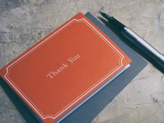 Orange thank you card with a white pen on a marble table