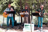 three men playing in a band next to the blue river