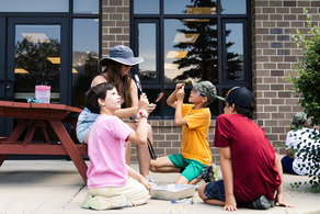 three kids and camp counselor outside with magnifying glasses