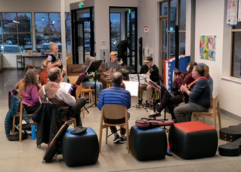 Residents sitting in a circle participating in a ukulele jam session at the Community Center