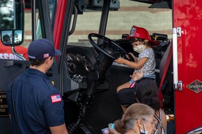 Child at the steering wheel of a firetruck staring at a fireman