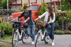 Two people with electric bikes talking in front of a truck full of flowers
