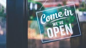 Photo of a 'come in we're open' sign hanging on a door.