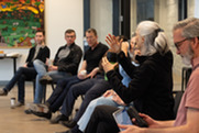 Person talking to group with a cup of coffee in her hand and people listening in the background during First Fridays.