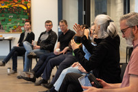 Person talking to group with a cup of coffee in her hand and people listening in the background during First Fridays.