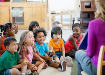 Kids sit in a group and listen to a teacher reading