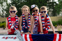 Kids sitting on a float smiling at the camera during the 4th of July parade.