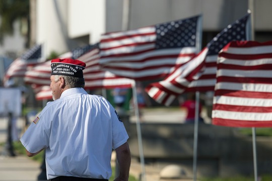 A veteran stands in front of a row of American Flags