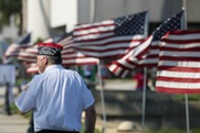 A veteran stands in front of a row of American Flags