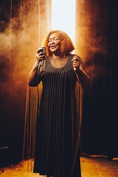 Hazel Miller singing with a heavenly gold mist behind her.