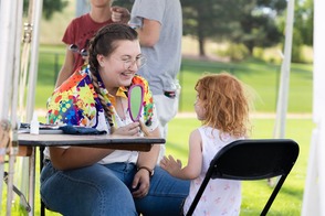 Woman showing a child their face paint after she compleated it.