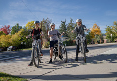 Three teens riding e-bikes with fall foliage in the background.