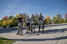 Three teens riding e-bikes with fall foliage in the background.