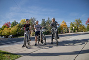 Three teens riding e-bikes with fall foliage in the background.