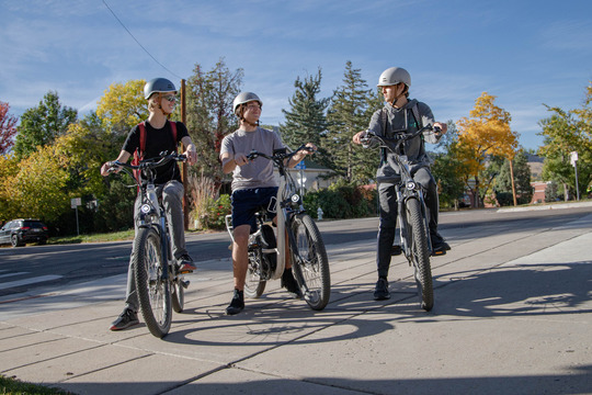 Three teens riding e-bikes with fall foliage in the background.