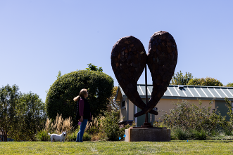 A woman and her dog admire the Angel Wings Sculpture in Founders Park.