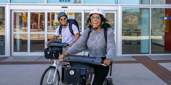Two people smile while riding electric bikes