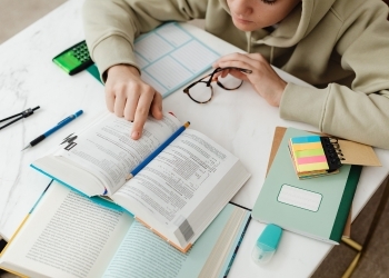 Person reading a book and surrounded by study materials