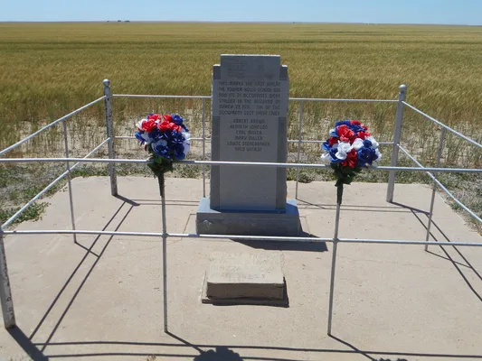 Monument with plains in the background, adorned with flowers.