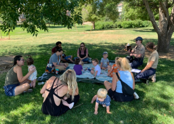 A group of parents and children sit in the grass during a Little Critters event