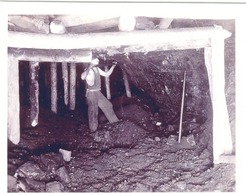 Black and white photo of miner deep in the mines picking at coal.