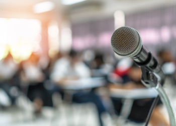 A microphone in focus in the front of a room of people