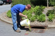 A person dumps paint water down a stormwater drain