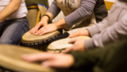 Several people play the drums with their hands in a circle
