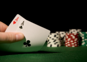 A hand holds two cards with poker chips in the background