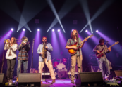 Six members of the Alcapones band perform on stage with purple lights.
