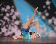 A young girl in a blue outfit contorts during a tumbling routine