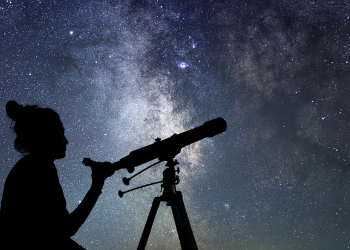 The silhouette of a person with a telescope and a starry sky backdrop 