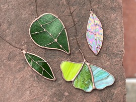 stained glass sun catchers in the shape of leaves sit against a pink cement background