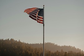 american flag blowing in the wind against an evening backdrop with clear skies and rolling hills of trees
