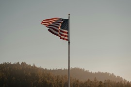 american flag blowing in the wind against an evening backdrop with clear skies and rolling hills of trees