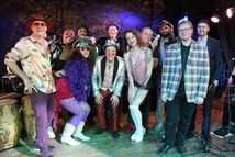 Members of The Pamlico Sound pose together on stage in colorful, retro-inspired outfits that reflect their funky, high-energy style.