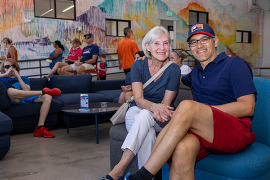 a woman and man pose for a photo on the SCC comfy chairs with people in 4th of july regalia milling around behind them