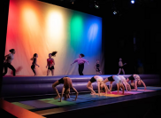 group of dancers perform bridge poses in front of a rainbow colored background