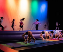 group of dancers perform bridge poses in front of a rainbow colored background