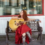 Singer Rebecca Folsom sits on a bench with her guitar 
