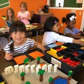 5 girls in a classroom using legos to create minecraft trees, creatures, and lettering saying "minecraft"