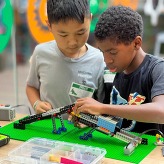 2 boys working together to create a spaceship or other craft using lego robotics