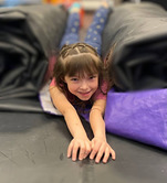 a girl smiles laying on her stomach in between 2 large cheerleading mats