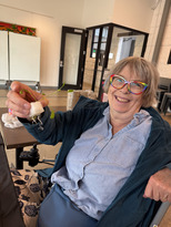 senior woman with rainbow colored glasses holds up a plant sprout for the camera at gardener's unite